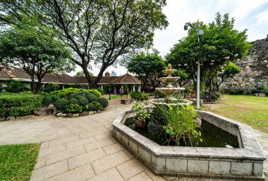 Bitkileri, çeşmeleri ve binaları olan yeşil bahçe.