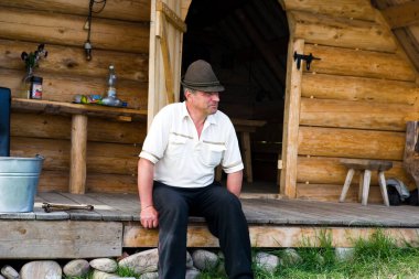 Ahşap evin yanında yetişkin bir adamın portresi.