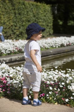 Parkta çiçeklerin yanında şapkalı bir çocuk.