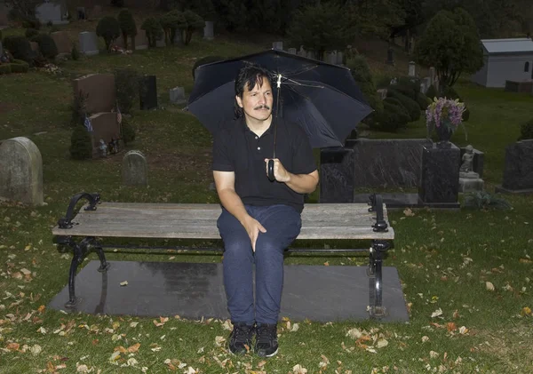 Hispánský Muž Sedí Lavičce Drží Deštník Hřbitově — Stock fotografie