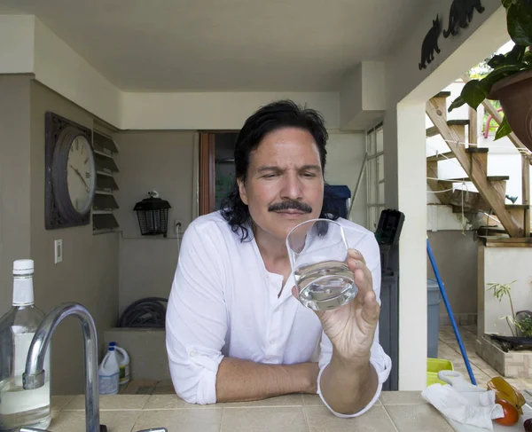 Hombre hispano mirando y sosteniendo un vaso de agua . — Foto de Stock