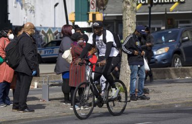 BRONX, NEW YORK / USA - 20 Mayıs 2020: Bir adam maskesiz bisiklet sürerken, diğerleri COVID-19 salgını sırasında otobüs bekliyor. 