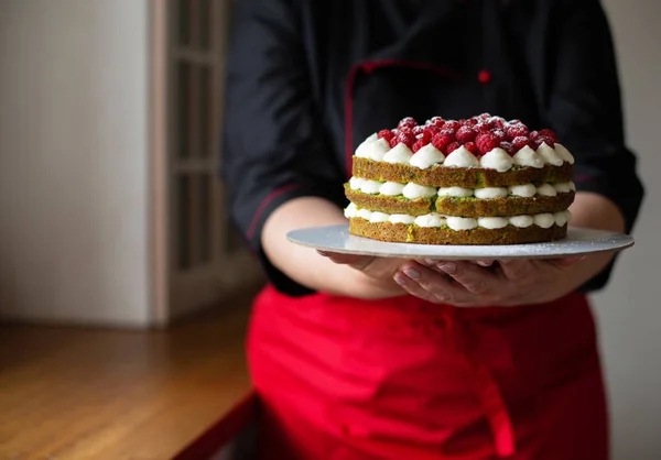 Confectioner in  Red-Black  Work Uniform Adorns the Cake with Berries  in the Kitchen. Confectioner, Cake, Cooking. Copy Space