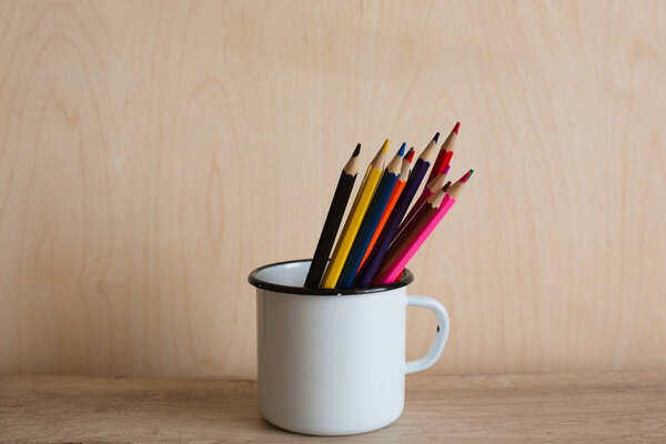 Цветные карандаши в чашке на деревянном фоне
