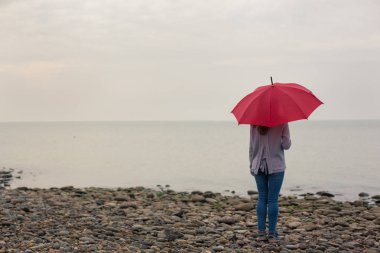 Issız sahilde kırmızı şemsiye olan kadın. Yalnızlık kavramı.  