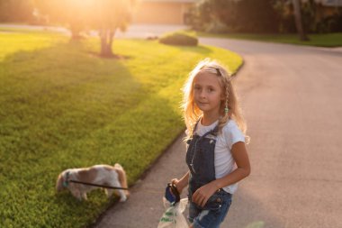 Sevimli Küçük kız Beautiful Sunset sokakta köpek yürüyor. Evcil hayvanla yürümek. Mutlu çocuk köpek yavrusu ile açık havada eğlenceli oynamak. Yaz günlerinde keyfini çıkarın. 