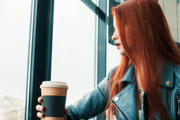 beautiful lonely young girl in a cafe drinks coffee. pretty red-haired girl thoughtful