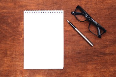 on table is an ink pen, glasses and a white sheet of notepad