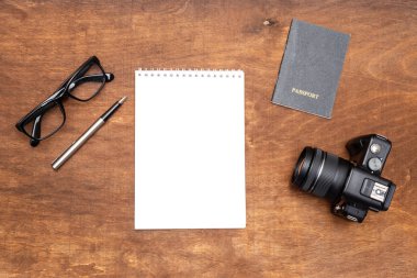 masada bir tükenmez kalem, gözlük ve Not defteri, pasaport, kamera beyaz bir levha var