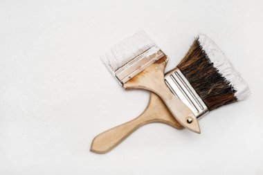 Two paint brushes lie on a white textured surface