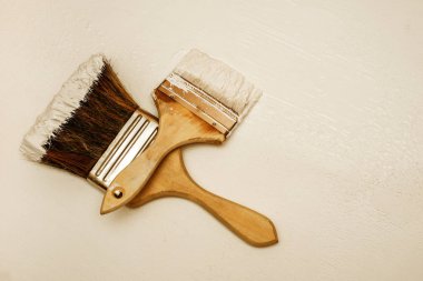 Two paint brushes lie on a white textured surface