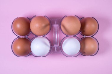 Plastik bir paket, pembe bir arka plan üzerinde beyaz ve kahverengi tavuk yumurtası