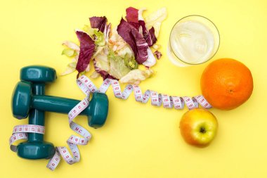 Halter sporu. Fitness salata ve şerit metre sarı bir tablo. Portakal, elma ve buz için sağlıklı bir yaşam tarzı kavramı ile temiz su.