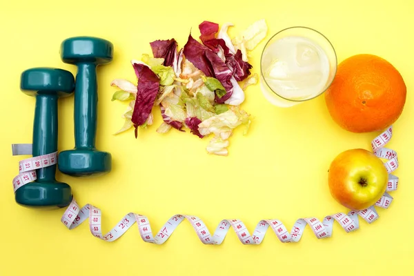 Dumbbells for sports. Fitness salad and tape measure on a yellow table. Oranges, apples and clear water with ice for the concept of a healthy lifestyle.