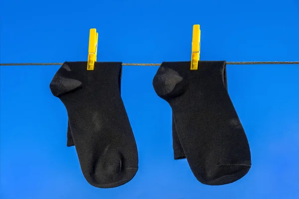 two new, clean, washed, black sock hang on a rope with yellow clothespins. blue sky background