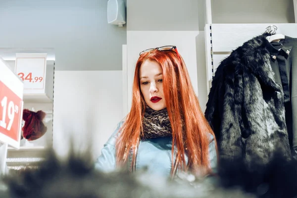 Retrato de niña de pelo rojo en una chaqueta de cuero azul. mujer en la tienda elige un abrigo de piel . —  Fotos de Stock