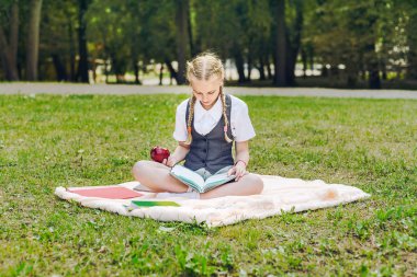 üniformalı öğrenci öğle yemeği için kırmızı elma yiyor. kız öğrenci kitapları ile bir parkta bir battaniye üzerinde oturan 