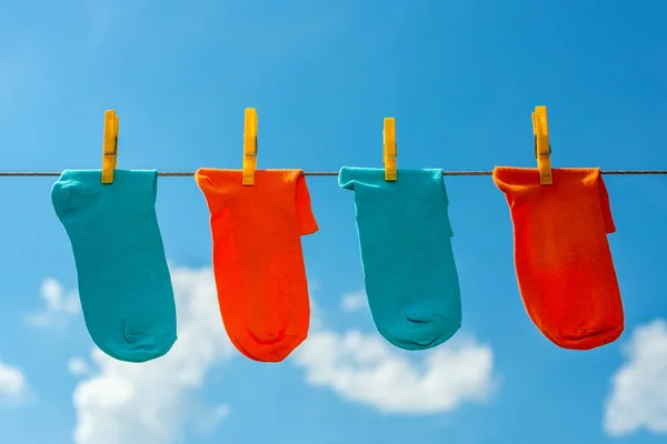 four new, clean, washed blue and orange socks hang on a rope with yellow clothespins.