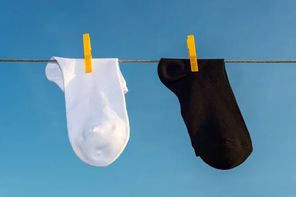 two new, clean, washed, orange socks hang on a rope with yellow clothespins.