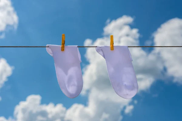 two new, clean, washed,  socks hang on a rope with yellow clothespins.