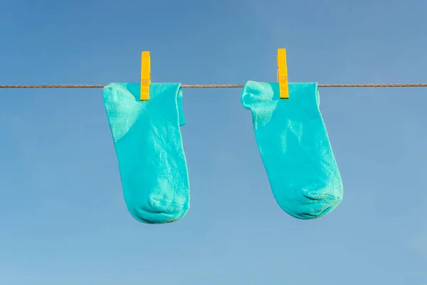 Two new, clean, washed blue socks hang on a rope with yellow clothespins