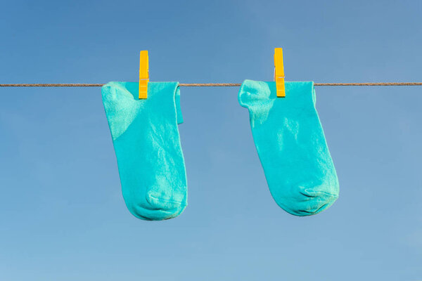 Two new, clean, washed blue socks hang on a rope with yellow clothespins 