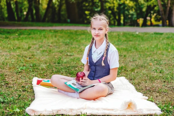 Портрет школьницы-подростка с косичками, сидящей в парке на покрывале с яблоком — стоковое фото