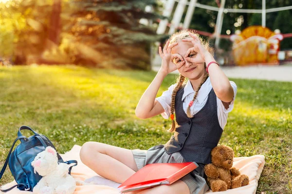 Μαθήτρια χαρούμενο χαμογελαστή και δείχνοντας εντάξει πινακίδα. ο μαθητής κάθεται σε ένα πάρκο σε μια κουβέρτα με μαλακά παιχνίδια παιχνίδι η αρκούδα κρατά — Φωτογραφία Αρχείου