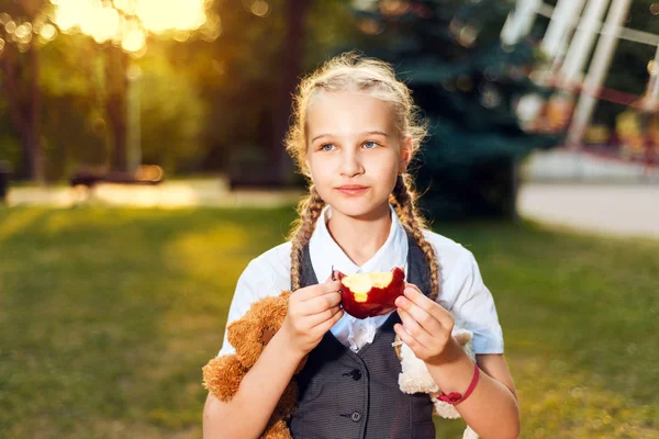 Μαθήτρια με κοτσίδες με τη στολή τρώει ένα μήλο στο πάρκο — Φωτογραφία Αρχείου