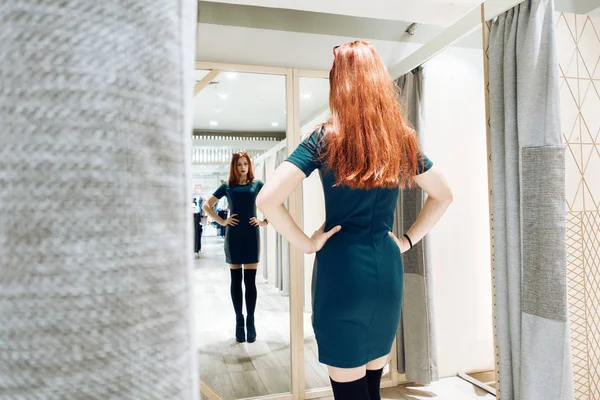 Молодая красивая девушка примеряет новое зеленое платье в примерочной в бутике . — стоковое фото
