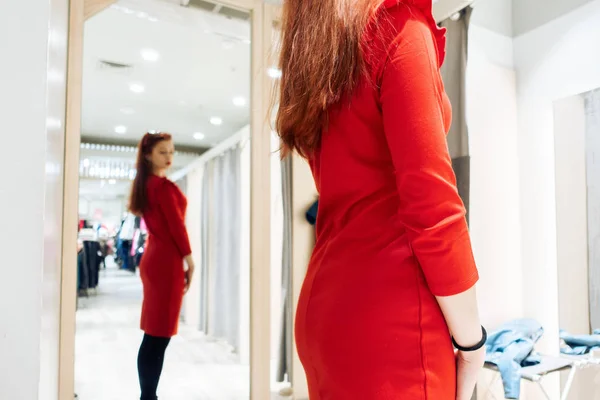 Молодая девушка примеряет красное платье в бутике прилегающей комнаты. Женщина покупает одежду в магазине . — стоковое фото