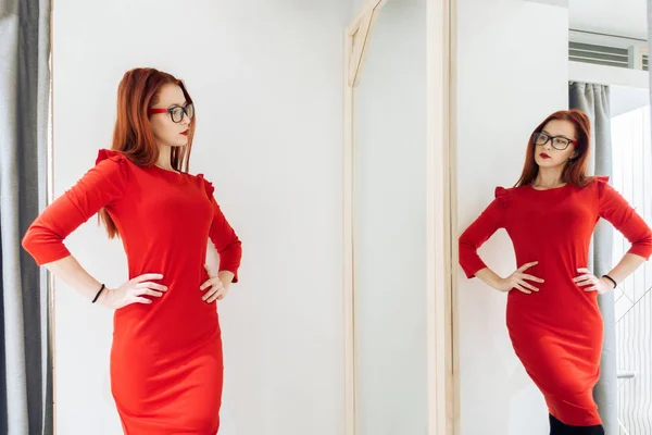 Красивая женщина примеряет одежду в примерочном магазине. дама в красном платье отражается в зеркале . — стоковое фото