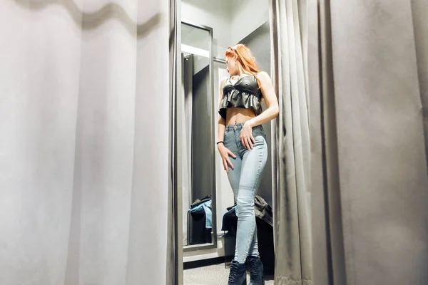 Юная стройная девушка примеряет новые джинсы в примерочной в магазине. женщина с красивой фигурой смотрит на себя в зеркало. покупка — стоковое фото