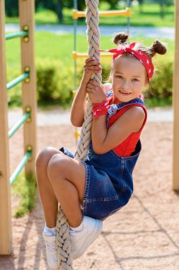 denim tulum ve kırmızı bir t-shirt ve eşarp küçük kız çalış ve oyun alanında eğleniyor