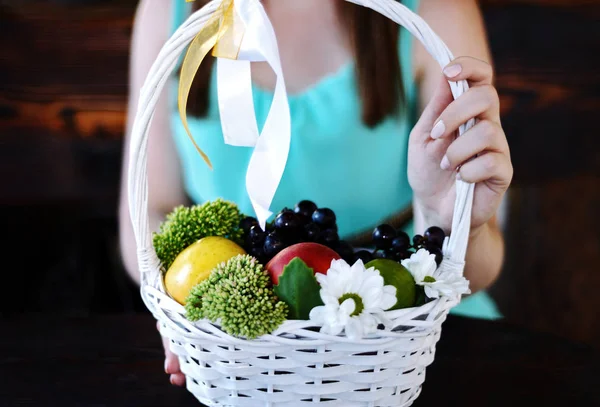 beautiful girl in a blue dress is holding a basket with fruits and flowers. concept of healthy eating