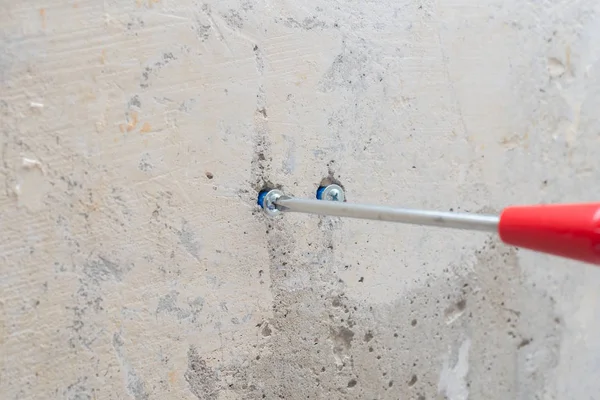 Red screwdriver twists the screw into the wall — Stock Photo, Image