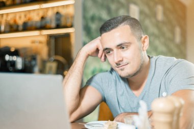 Bir kafede genç adam çalışıyor. adam gülümsüyor ve dizüstü bilgisayariçine bakar