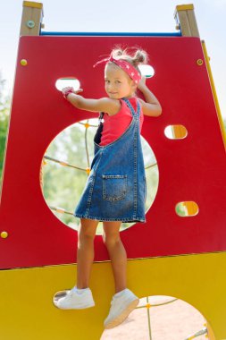 Kot pantolonlu, saç stili kuyruklu küçük kız tırmanıyor.