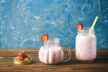 Konserve kapağında olgun çilekler. Tahta bir masada, taze, cam çilekli smoothie 'nin içinde. mavi arkaplan