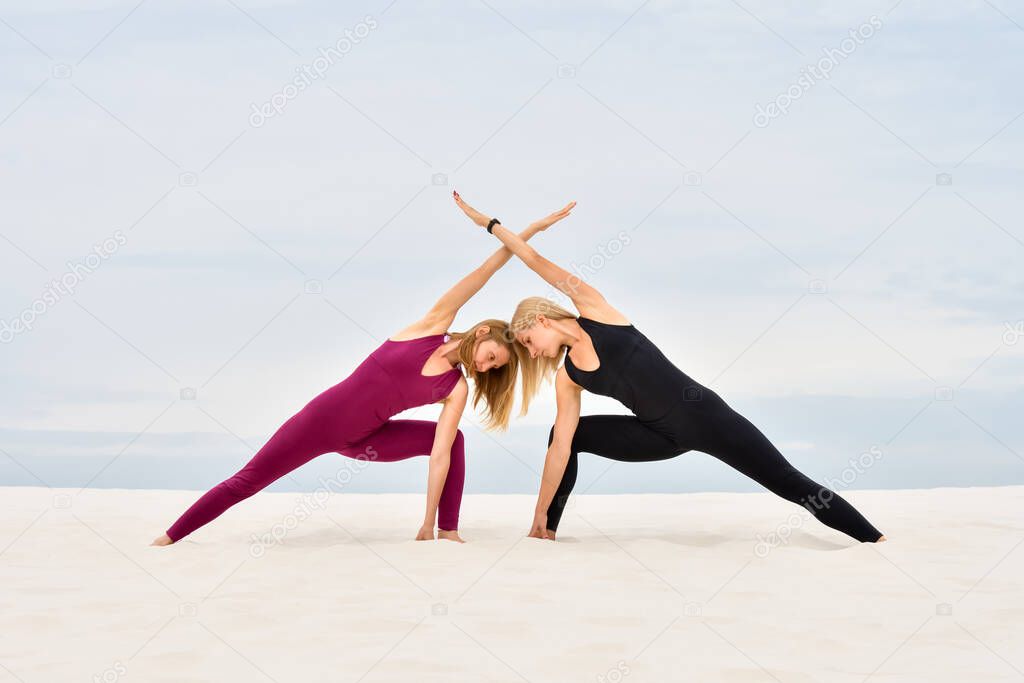 Two beautiful young women performing together yoga pose parshvakonasana