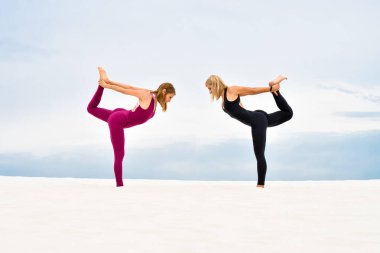 Yoga yapan iki güzel genç kadın sahilde nataradzhasana pozu veriyor.