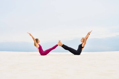 İki güzel genç kadın yoga pozu veriyor Navasana.
