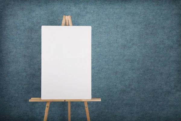 Wooden easel with blank canvas against a blue wall