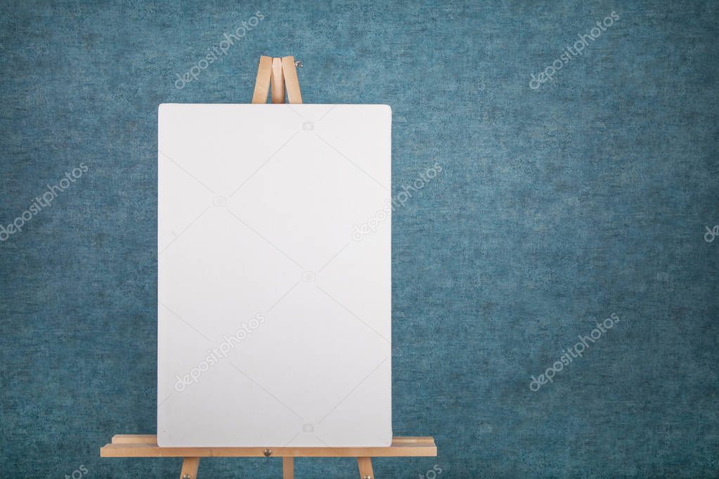 Wooden easel with blank canvas against a blue wall