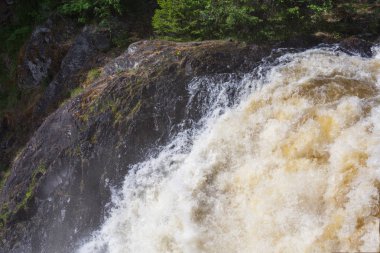 Su acele Streams kayaların arasına çalıştırıyor. Beyaz Köpük ve Sprey Güneş parıldıyor. Yeşil orman taş kıyısında büyür. Gökyüzü mavi rengini suya yansıtılır. Kivach şelale. Karelya. Rusya.