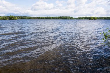 Göl güzellik. Mavi gökyüzünün suya yansıtılır. Rüzgar küçük bir dalgalanma gölün yüzeyi boyunca döner. Yeşil ağaçlar su için inerler. Plaj taş Dağları'nın kalıntıları oluşur. Konchozero. Karelya. Rusya.