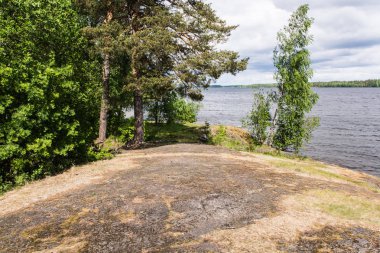 Göl güzellik. Mavi gökyüzünün suya yansıtılır. Rüzgar küçük bir dalgalanma gölün yüzeyi boyunca döner. Yeşil ağaçlar su için inerler. Plaj taş Dağları'nın kalıntıları oluşur. Konchozero. Karelya. Rusya.