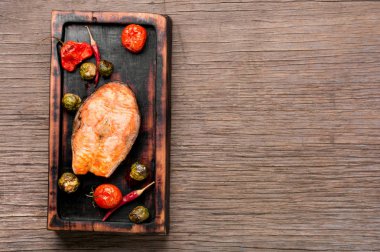 Domates, biber ve kabakla pişirilmiş somon balığı. Ahşap retro arka planda balık yemi.