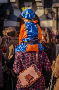 Dordrecht, Hollanda - 17 Kasım 2018: genç çocuk oturan geçmek Saint Nicolaas için beklerken bir üst omuz Pete Sinterklaas, bir turuncu ve mavi kostüm giymiş.