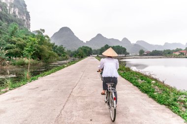 Geleneksel konik hasır şapka bisiklet üzerinde Vietnamca kadınla. Pirinç tarlaları ve dağ doğa sahne güzel manzara rezerv Trang bir ve Tam Coc, Ninh Binh Eyaleti, Vietnam
